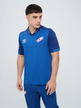 Remera polo deportiva Umbro del Club Nacional de Football, color azul con cuello en V y detalles en rojo y blanco. Incluye el logo de Umbro y el escudo del club.