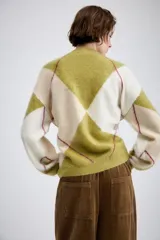 Chaqueta de punto con diseño de rombos en tonos verde oliva y crema, con cuello redondo, cierre frontal de botones y mangas largas con puños ajustados.