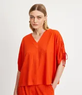 Blusa amplia color naranja, con escote en pico y mangas cortas con detalle de lazo fruncido.