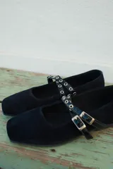 Ballerina de gamuza negra con puntera cuadrada y doble tira cruzada en el empeine con ojales metálicos y hebillas ajustables.