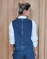 Chaleco de corte recto y largo a la cintura, confeccionado en denim con estampado de rayas verticales en tonos azul y blanco. Presenta cuello redondo y costuras visibles que definen su estructura.