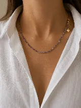 Collar de cuentas pequeñas en tono violeta con detalles metálicos, cierre de cadena con dije de corazón dorado.