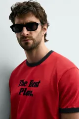 Camiseta de corte regular color rojo con cuello redondo y bordes de mangas en color azul marino. Presenta una estampa frontal con la frase 'The Best Plan.' en color azul marino.