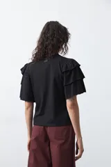 Remera negra de algodón con cuello redondo y mangas cortas con volados en capas que aportan volumen y movimiento.