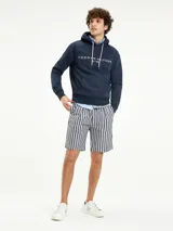 Hoodie azul marino de Tommy Hilfiger con capucha ajustable mediante cordones blancos. Presenta un bolsillo tipo canguro en la parte frontal y el logo de la marca bordado en el pecho junto a la inscripción 'EST. 1985'.