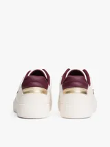 Zapatillas de cuero estilo tenis, color blanco, con cordones y suela de goma al tono. Presentan forro interior en color bordó, ojal superior metálico dorado y logo de monograma TH metálico en el lateral.
