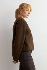 Chaqueta reversible de corte recto con cierre frontal de cremallera. Presenta un lado en acabado de gamuza negra y el reverso en tejido de textura tipo corderito color marrón chocolate, con cuello redondo y bolsillos frontales.