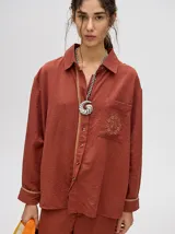 Camisa azul de corte holgado, con cuello camisero, mangas largas con detalles en los puños, bolsillo frontal con bordado y cierre delantero con botones.