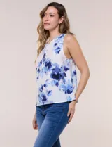 Blusa sin mangas de viscosa blanca con estampado floral en tonos azules, cuello redondo y cierre frontal parcial con botones.