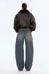 Jean de cinco bolsillos en denim de algodón rígido, color azul oscuro con efecto desgastado. Modelo de cintura clásica con cierre y botón, corte holgado y piernas anchas tipo barrel con costuras laterales marcadas.