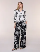 Conjunto de camisa y pantalón amplio con caída fluida. Camisa con escote en V y abotonadura frontal, mangas largas de corte caído con detalle de puntilla calada y puños elastizados fruncidos. Pantalón de tiro alto con cintura elastizada, pierna holgada de corte wide leg con dobladillo ancho en el ruedo y bolsillos laterales.