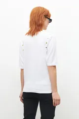 Remera blanca de manga 3/4 con cuello redondo y botones metálicos decorativos en los hombros.