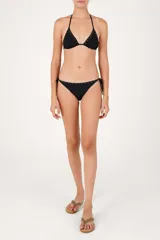Calzón de bikini de tiro bajo color negro, con laterales de lazos ajustables con cuentas decorativas y una hilera de pequeños aros metálicos dorados en el borde superior.
