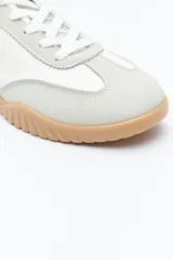 Zapatilla urbana de mujer con silueta retro, combinando paneles de cuero blanco y gamuza gris claro. Posee un talón trasero en gamuza negra y suela robusta de goma color caramelo con relieve.