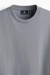 Remera gris de corte relajado, confeccionada en punto liviano con cuello redondo ribeteado, hombros caídos y mangas cortas.