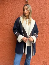Saco de paño azul marino con solapas amplias y puños en corderito sintético color crema. Presenta detalles en cuero sintético marrón en la parte frontal y en las mangas, con un diseño abierto y corte recto.