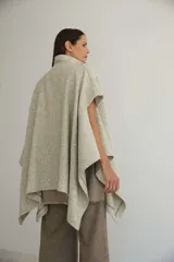 Capa de lana fina con cuello alto, cierre frontal con botones ocultos y bolsillos plaqué. Presenta aberturas laterales versátiles que permiten usarla como poncho o ruana, con terminaciones envivadas.