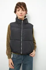 Chaleco puffer color beige, sin mangas, con cuello alto y cierre frontal con cremallera.