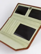 Billetera combinada de cuero en tonos marrón y camel, con solapa frontal de pelo vacuno estampado y detalle de placa con el logo de la marca.