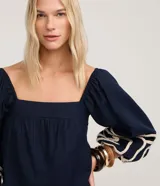 Blusa corta azul marino con escote recto estilo hombro a hombro, mangas largas abullonadas con detalle de bordado decorativo en cuerda clara.