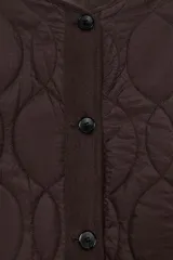 Cazadora corta acolchada de color negro, con cuello redondo, manga larga y cierre frontal con botones. Presenta un diseño de costuras geométricas y bolsillos laterales de vivo.