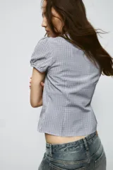 Camisa de algodón con estampado de cuadros, cuello solapa, mangas cortas abullonadas y detalle de fruncido elástico en el pecho. Cierre frontal con botones.