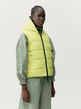 Chaleco reversible con capucha, confeccionado en tejido repelente al viento con relleno vegano. Presenta cierre frontal de doble cursor, bolsillos laterales con cierre y sisas con terminación en vivo.