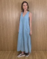 Vestido largo de denim celeste, sin mangas, con escote en V, corte amplio, bolsillos laterales y tajos pronunciados en la parte inferior con detalles de pespuntes.