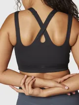 Top deportivo negro de sujeción media, confeccionado en tejido suave y elástico con Aloe Vera. Presenta un diseño de espalda cruzada y dos tiras con aberturas en los hombros.