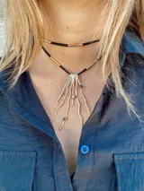 Gargantilla con doble collar de cuero negro y detalles dorados. El collar inferior tiene un colgante con forma de rama dorada y piedras incrustadas.