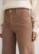 Pantalón de pana color tostado con corte wide leg y tiro alto. Presenta diseño clásico de cinco bolsillos, cierre frontal con botón y una caída recta y amplia.