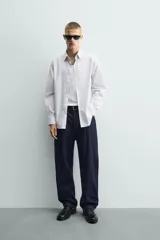 Camisa de corte regular fit confeccionada en tejido de algodón con diseño de rayas verticales finas. Presenta cuello italiano, manga larga con puños abotonados y cierre frontal mediante botonadura.