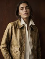 Jacket de cuero color camel con acabado envejecido, diseño estructurado con solapas, cierre frontal con broches a presión y bolsillos frontales con solapa.