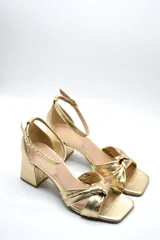 Sandalia de tacón medio ancho con diseño de nudo frontal y pulsera ajustable al tobillo con hebilla metálica.