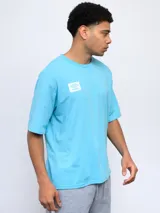 Remera de corte holgado color celeste, con cuello redondo diferenciado y logo de la marca estampado en el pecho. Presenta un diseño de manga corta y estilo deportivo.