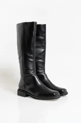 Botas de caña media confeccionadas en cuero vacuno, con diseño de punta redondeada y suela plana con pequeño taco cuadrado. Presentan costuras verticales decorativas a lo largo de la caña.