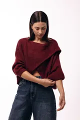 Sweater de punto con diseño cruzado frontal, de silueta amplia y mangas largas con puños ajustados. Presenta un corte holgado y textura suave.