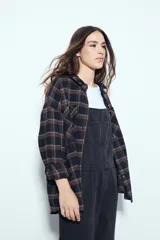 Camisa tipo leñadora de corte oversize, con estampado de cuadros en tonos negro y marrón. Presenta cuello clásico, cierre frontal con botones y mangas largas con puños abotonados.