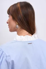 Blusa celeste con rayas verticales, cuello en V, mangas largas abullonadas con puños blancos y volantes verticales en el frente.