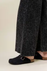 Pantalón de jean negro de pierna ancha y tiro medio-alto, con estampado sutil de leopardo en tono más oscuro y pequeños puntos blancos brillantes.