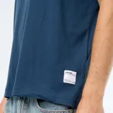 Remera de algodón color azul, de corte holgado, mangas cortas y cuello redondo. Cuenta con una pequeña etiqueta blanca decorativa en el borde inferior izquierdo.