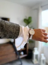Camisa blanca de estilo romántico con volados en el frente, detalles de encaje y mangas largas con puños elásticos. Presenta un diseño con alforzas en la parte inferior y cierre frontal con botones.