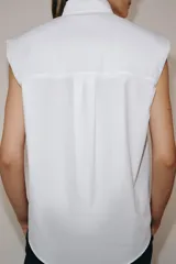 Camisa sin mangas confeccionada en algodón, con cuello redondo y detalle de lazada frontal. Presenta cierre frontal con botones ocultos por solapa y bajo redondeado.