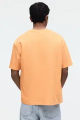 Remera de algodón de peso medio, color naranja, con cuello redondo ribeteado y hombros caídos de corte relajado.
