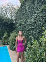 Vestido corto de satén color verde azulado (teal) con escote strapless y detalle de frunce central con argolla. Presenta tirantes finos que se atan al cuello y aberturas laterales en la cintura.