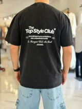 Remera oversize negra con efecto acid wash, mangas cortas y estampa tipográfica en la espalda con el texto 'The Top Style Club'.