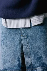 Falda midi de tiro medio confeccionada en denim con efecto lavado. Presenta cintura con trabillas, cierre frontal con cremallera, botón y gancho metálico, y una abertura en el bajo.