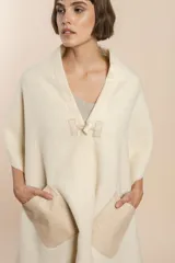 Chal de lana fina sin teñir con diseño de cuadros sutiles, cierre frontal con alamar y bolsillos de cuero metalizado. Presenta terminaciones con flecos en el ruedo y un calce estructurado en los hombros.