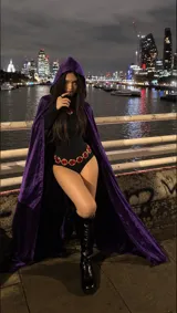 Disfraz de Raven que incluye body negro, capa con capucha de terciopelo morado, cinturón con gemas rojas y broche decorativo.