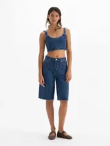 Bermuda de denim 100% algodón, tiro medio y calce recto, con diseño tradicional de cinco bolsillos y lavado azul intermedio con efecto gastado.